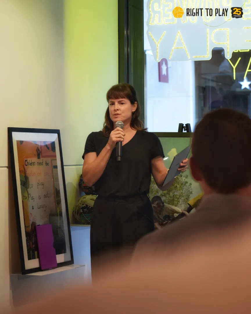Zoe Dibb stands on stage with a microphone, launching Right To Play's new Policy Brief