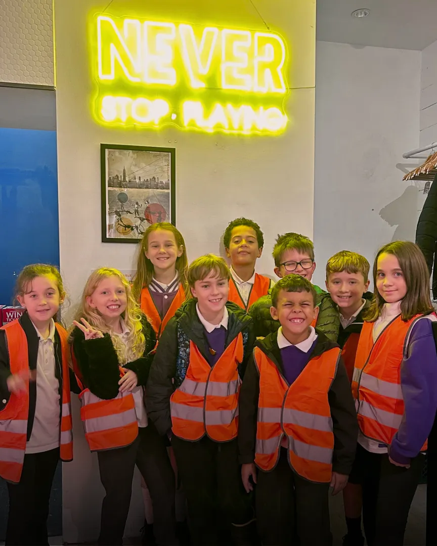 Students from Cooper's Lane school pose in front of a neon sign that says "Never Stop Playing"