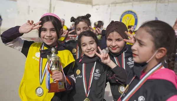 Four children wearing medals and athletic wear pose for a photo. One child holds a trophy and makes a peace sign with her fingers.